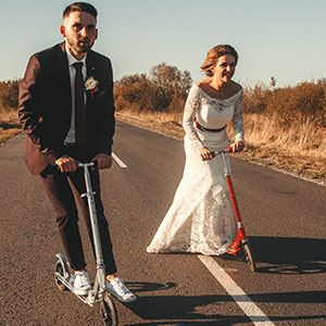 smiling wedding couple riding scooters along road outside city sunset