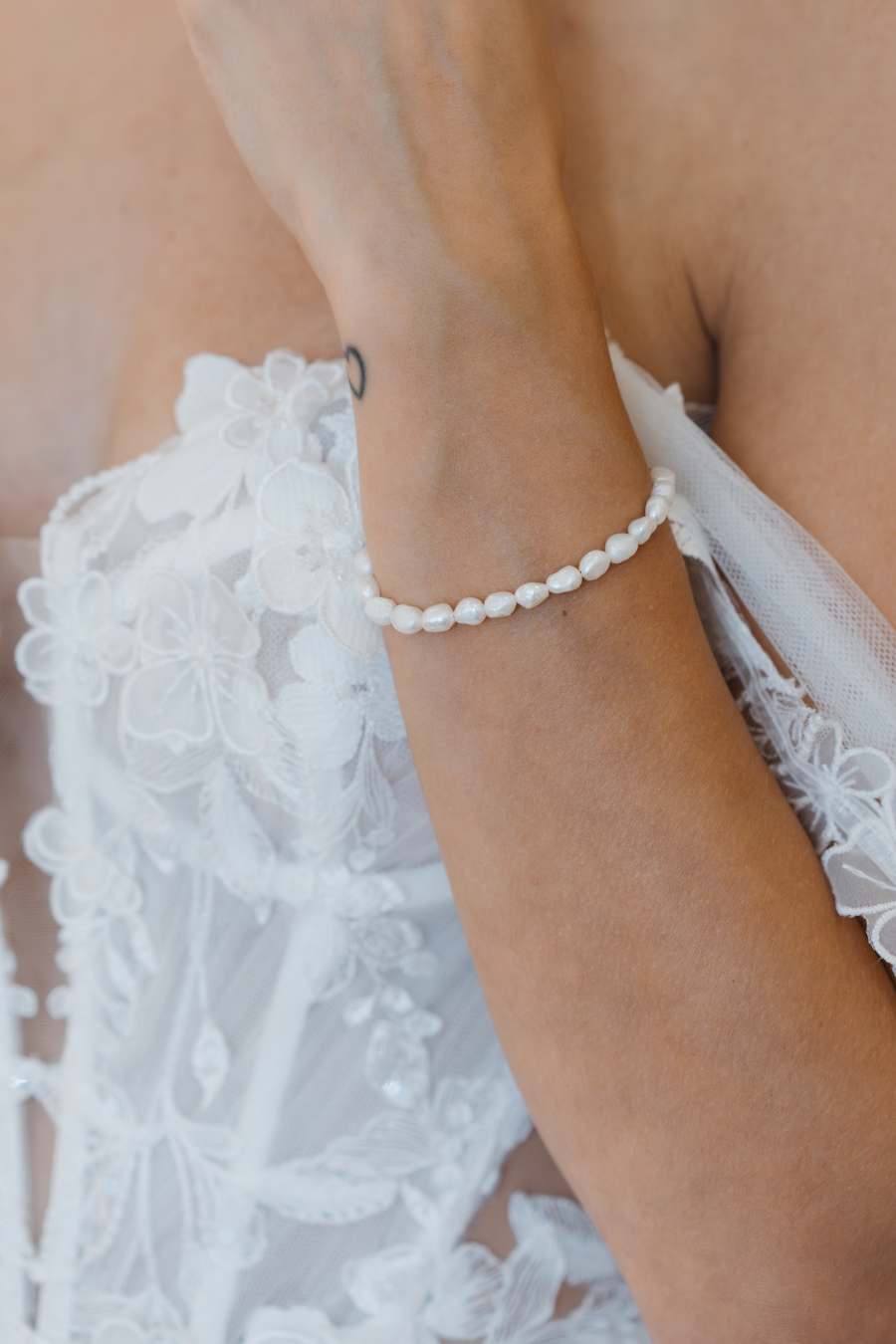 Feines Perlarmband am Handgelenk einer Braut im Spitzenkleid eleganter Brautschmuck von Novia Feliz für Hochzeiten in stilvollem Look