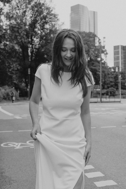 Braut in schlichter, moderner Robe von Novia Feliz lacht auf einer Straße in Frankfurt – natürlicher Moment mit urbanem Flair und Stil