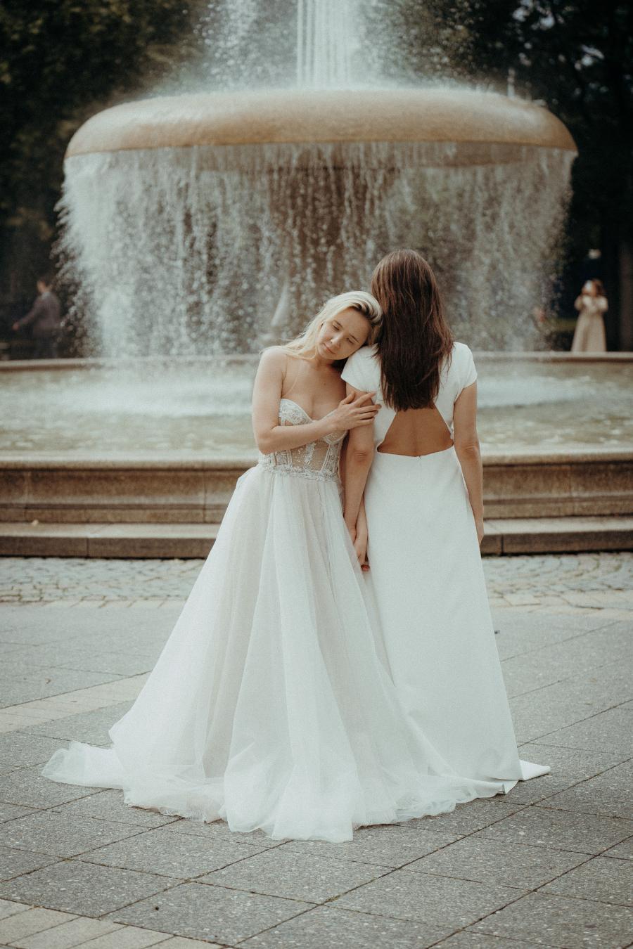 Zwei Bräute in exklusiven Brautkleidern von Novia Feliz vor Brunnen in Frankfurt – romantischer Moment mit professionellem Styling