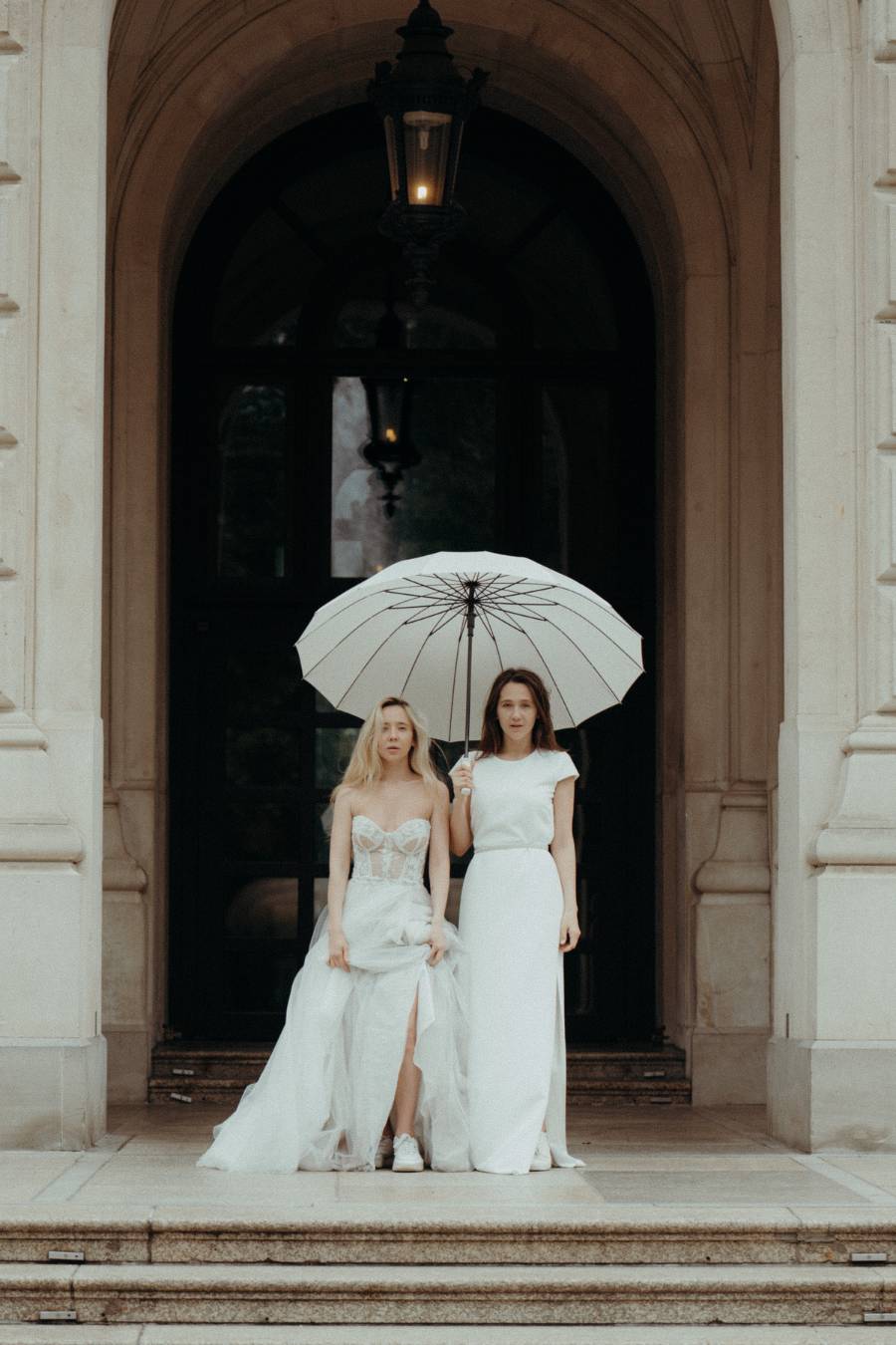 Zwei Frauen in weißen Kleidern mit weißem Schirm vor einem historischen Gebäudeportal
